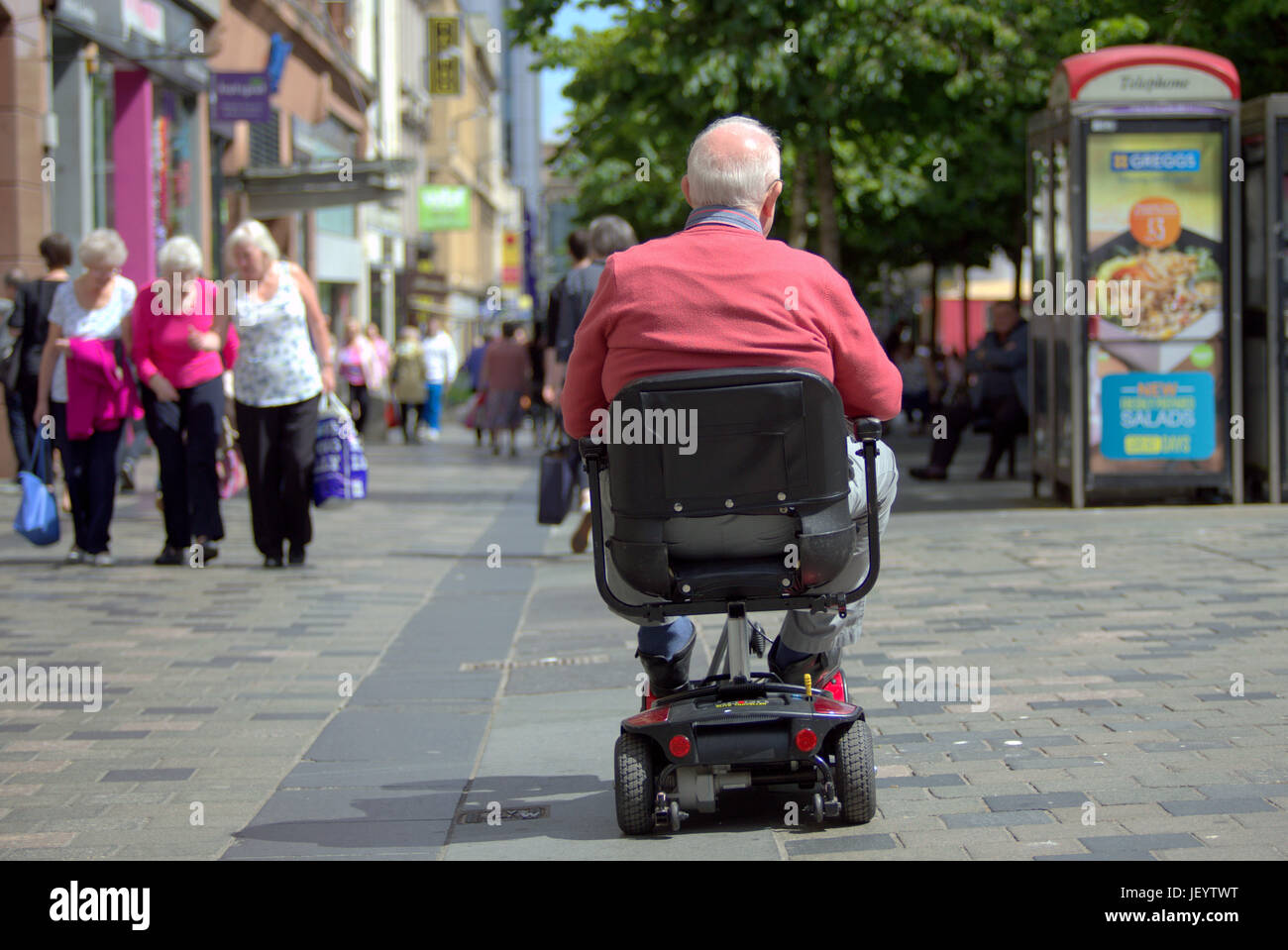 Senioren oder alten Menschen Senioren in Glasgow Schottland auf der Straße in ein Rollstuhlfahrzeug shopping Precinct rosa Strickjacke Stockfoto