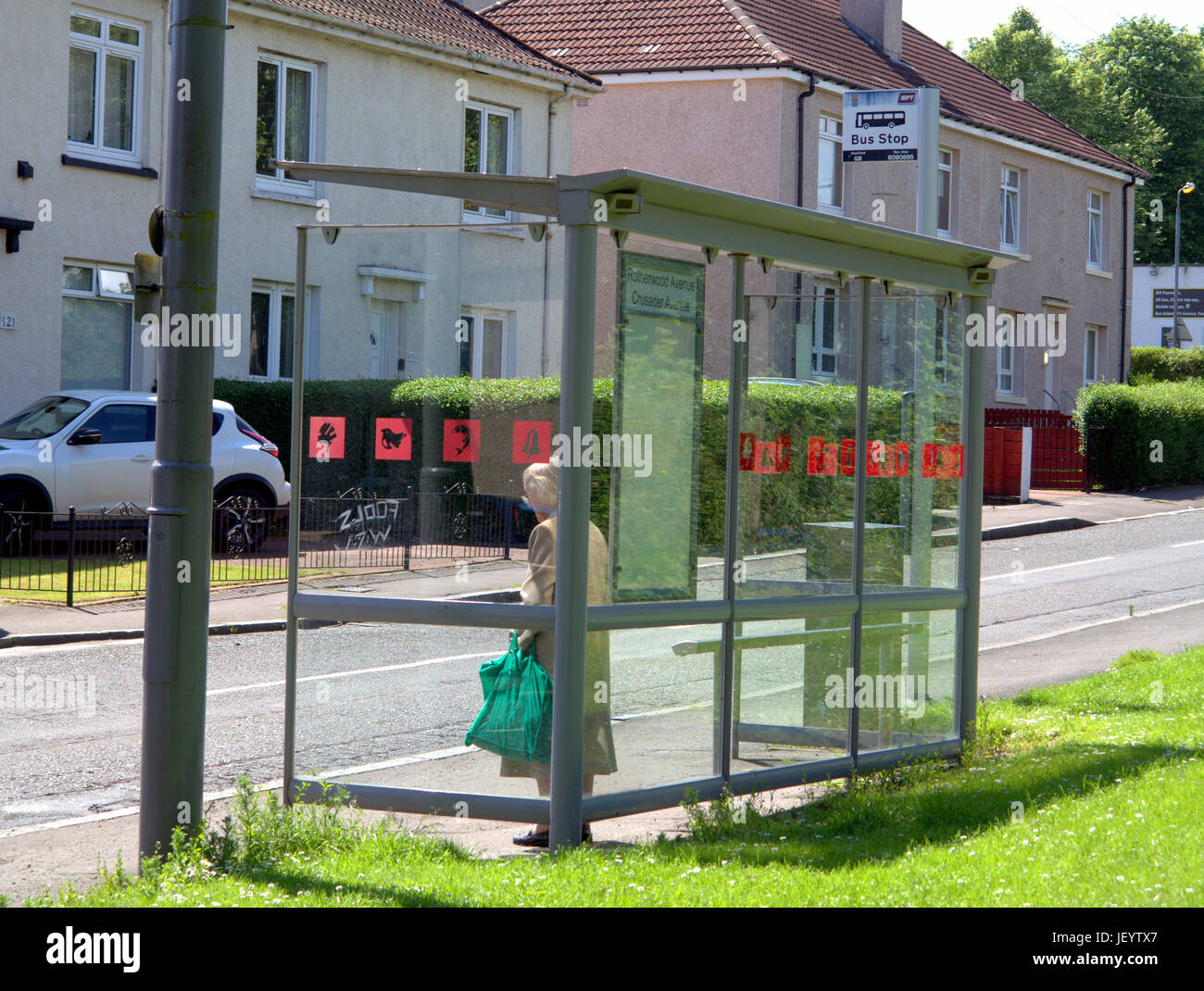 Senioren oder alte Person Senioren in Glasgow Schottland warten allein an einer Bushaltestelle Einkaufstaschen tragen Stockfoto