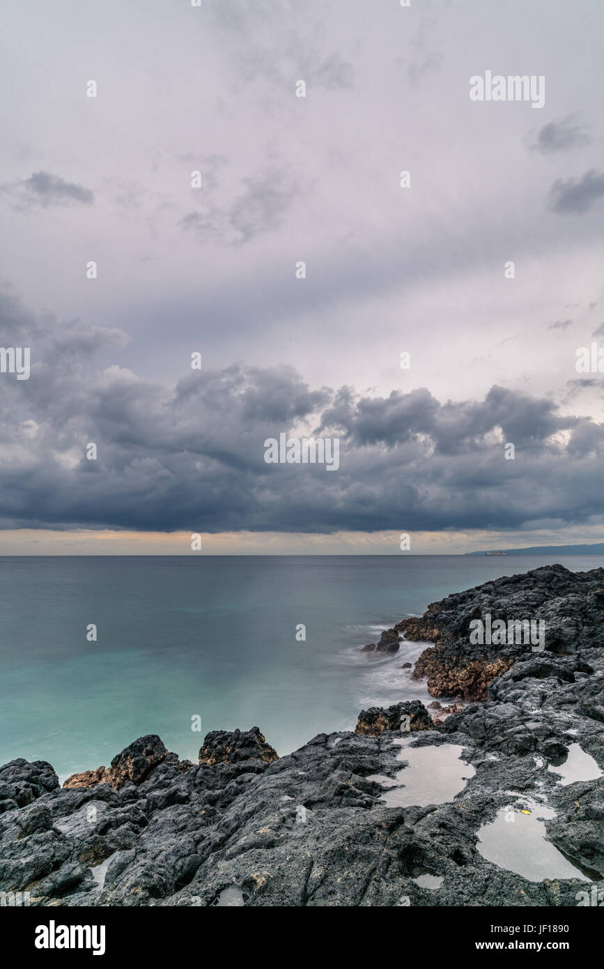 Dicke, schwere Wolken schweben über Meer und felsige Küste in Padangbai, Indonesien. Stockfoto