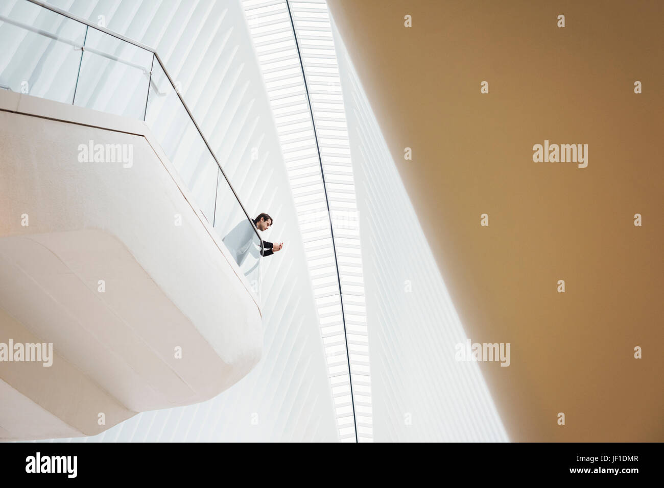 Blick von unten auf ein Mann steht auf einem Balkon in das Oculus Gebäude, Blick auf sein Handy. Balkone über dem Boden im Dachraum. Stockfoto