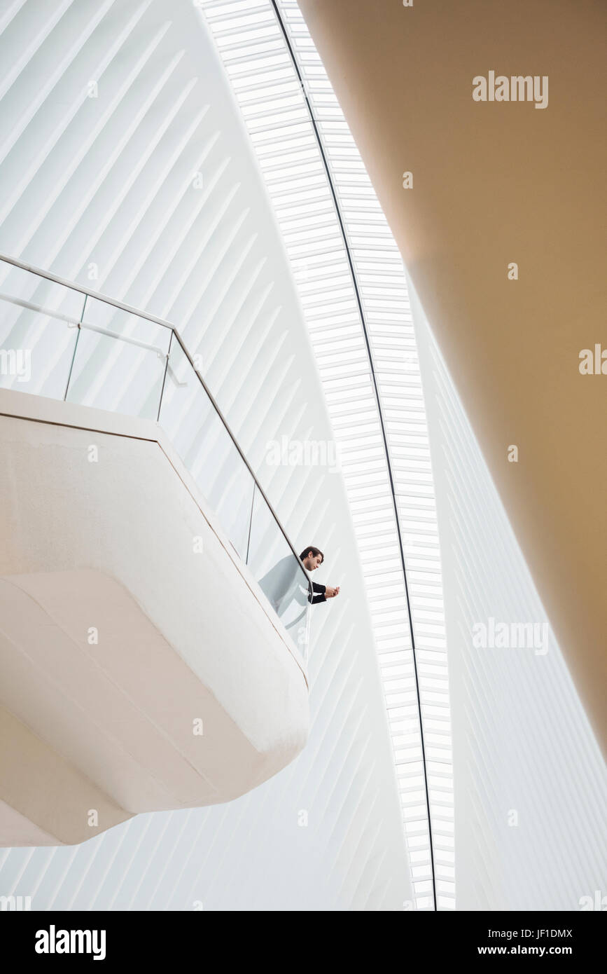Blick von unten auf ein Mann steht auf einem Balkon in das Oculus aufbauend auf seinem Telefon, stützte sich auf das Geländer.  Großen gerippten Dach Bogen über ihn. Stockfoto