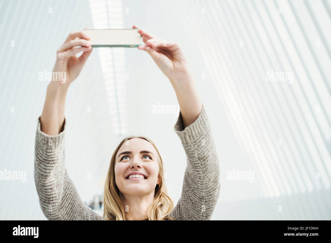 Eine junge Frau, die ein Foto mit ihrem Handy, gewölbten Dach eine selfy im World Trade Center Oculus Gebäude mit einem atemberaubenden weißen gerippt. Stockfoto