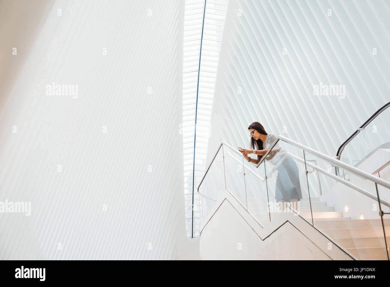 Eine Frau auf der Treppe, stützte sich auf ein Geländer in den weiten Raum des Atriums des Oculus-Gebäudes auf dem Gelände des World Trade Center in New York City. Stockfoto