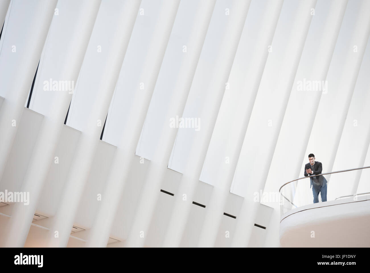 Eine Person, die allein in einem Atrium durch ein Geländer, unter einem hohen weißen zerfurcht Decke. Stockfoto