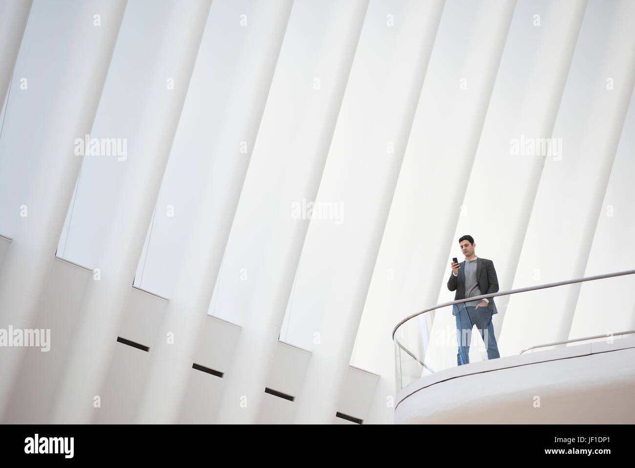 Eine Person, die allein in einem Atrium durch ein Geländer, unter einem hohen weißen zerfurcht Decke. Stockfoto