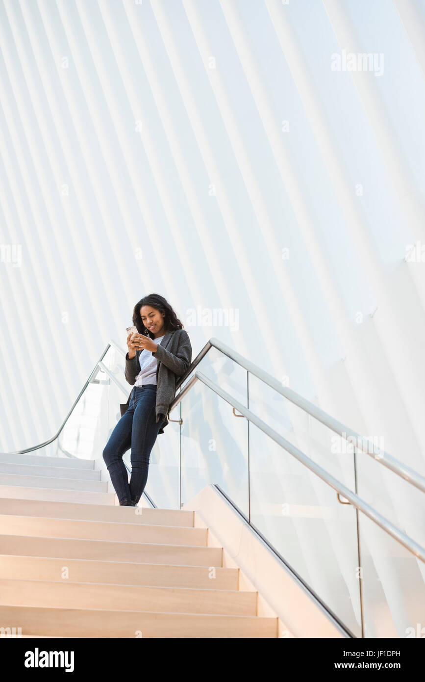 Eine Frau steht auf einer Treppe im Oculus Gebäude im World Trade Center unter einer dramatischen geriffelte weiße Decke, überprüft ihr Telefon. Stockfoto