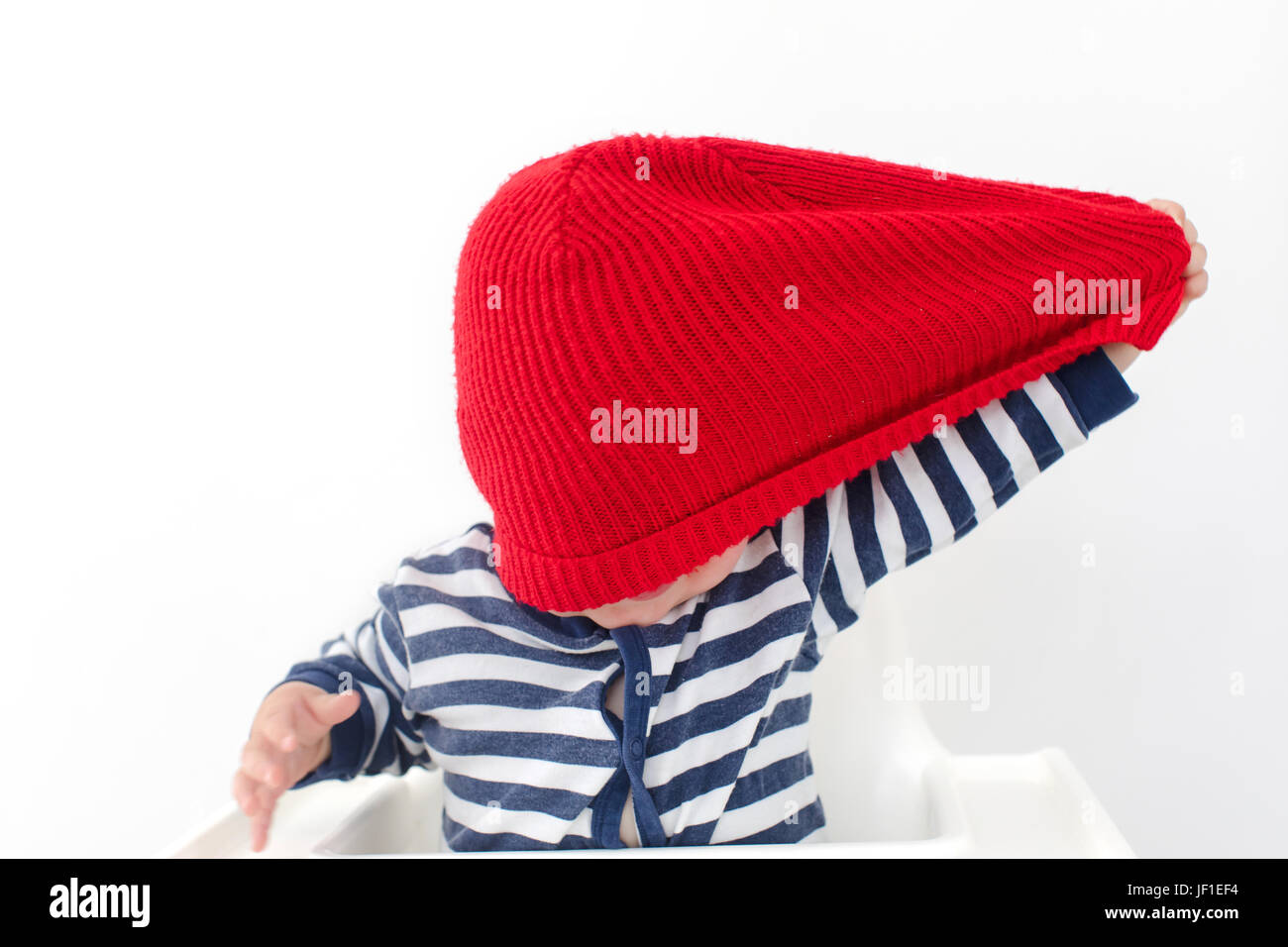 Kleinkind nimmt Hut in rote Kappe über Gesicht studio Stockfoto