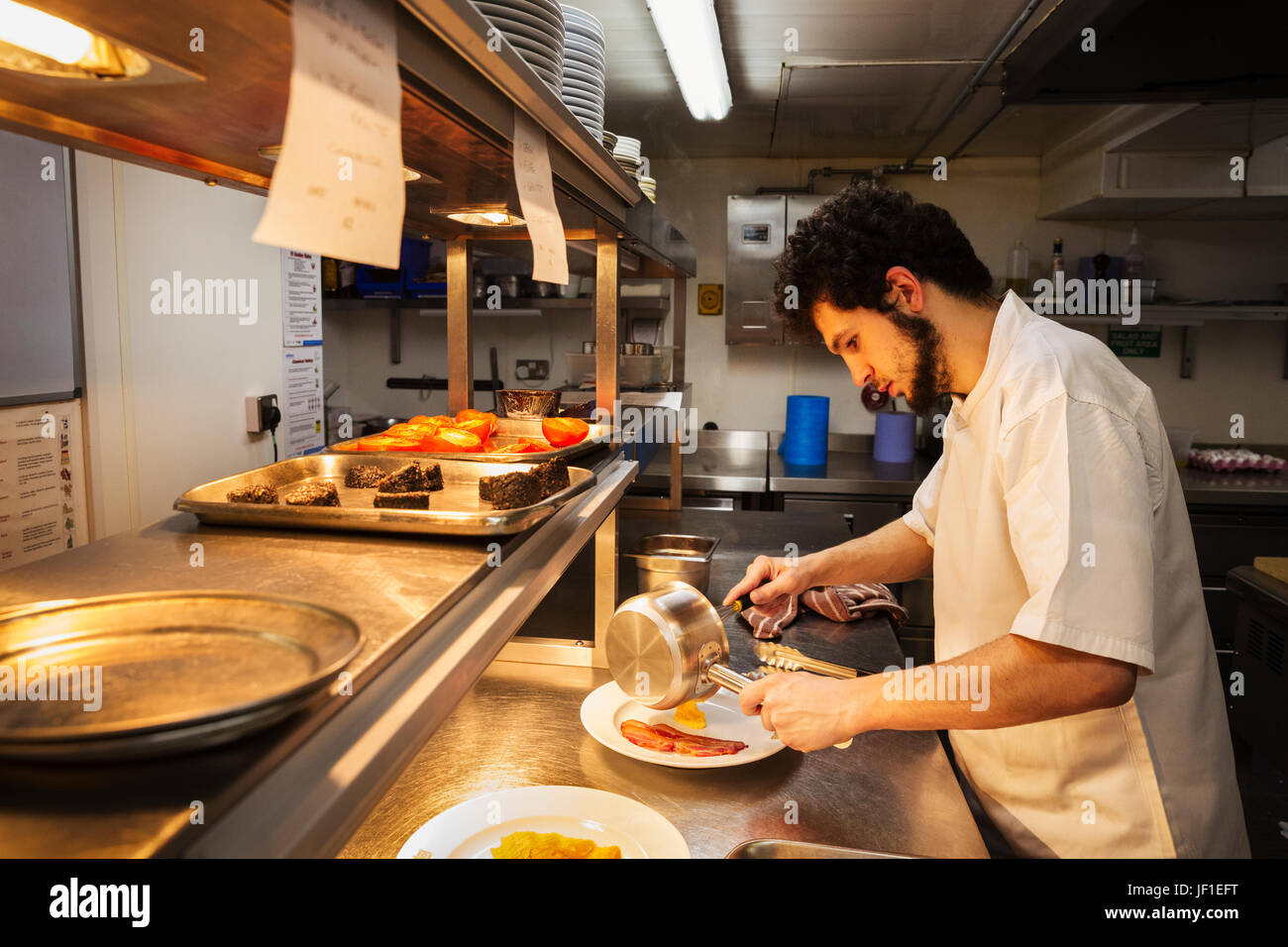Koch in einer Küche an einem Schalter stehen, hält Topf, Plattieren Essen. Stockfoto