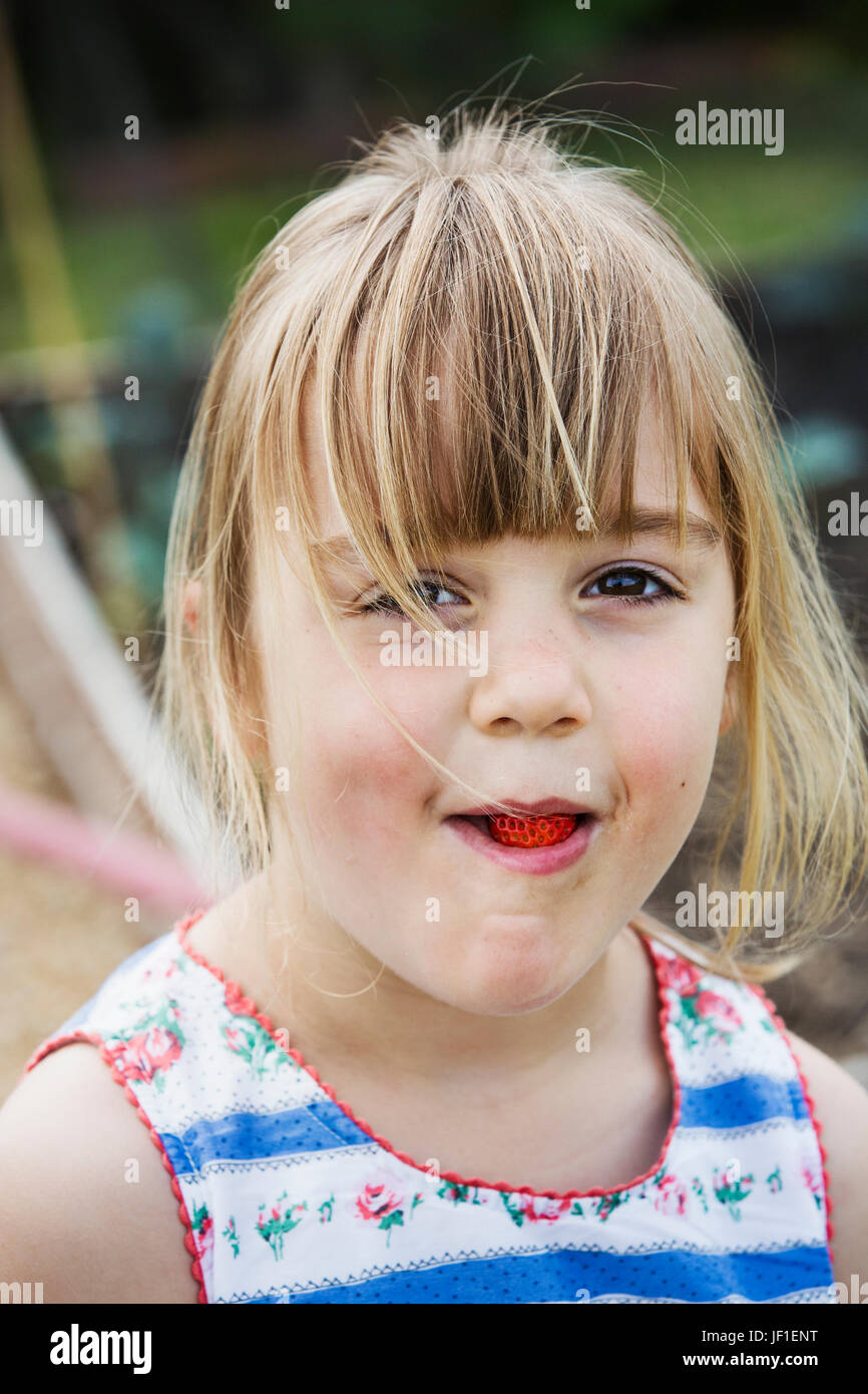 Lächelndes Mädchen essen eine Erdbeere, Blick in die Kamera. Stockfoto