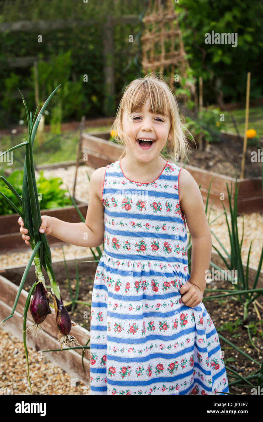 Lächelndes Mädchen in einem Sommerkleid in einem Garten stehen, hält ein Bündel von Zwiebeln, Blick in die Kamera. Stockfoto