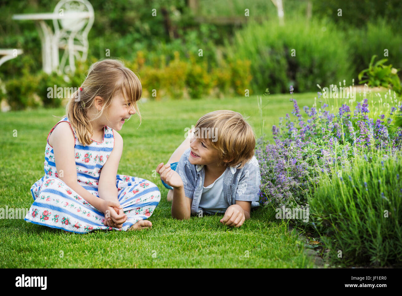 Ein Mädchen sitzt auf dem Rasen im Gespräch mit ihrem Bruder lag neben ihr auf dem Rasen im Garten. Stockfoto