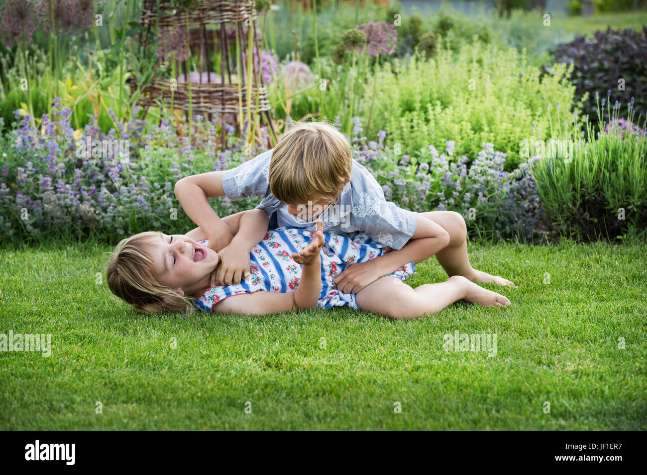Lächelnden jungen und Mädchen in einem Garten, Roughousing, zusammen zu spielen, Playfighting auf einer Wiese. Stockfoto