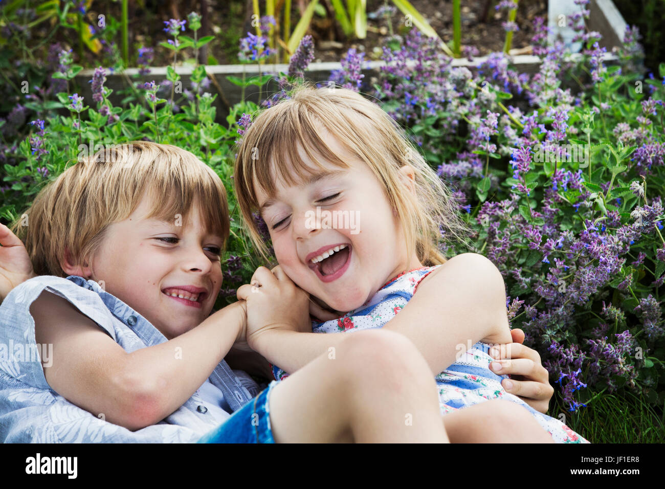 Lächelnde junge und Mädchen Roughousing, in einem Garten im freien zusammen zu spielen. Stockfoto