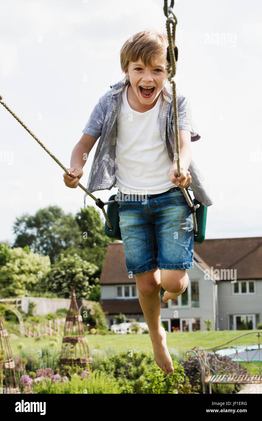 Lächelnde junge in Hemd und Jeans Shorts auf einer Schaukel im Garten. Stockfoto