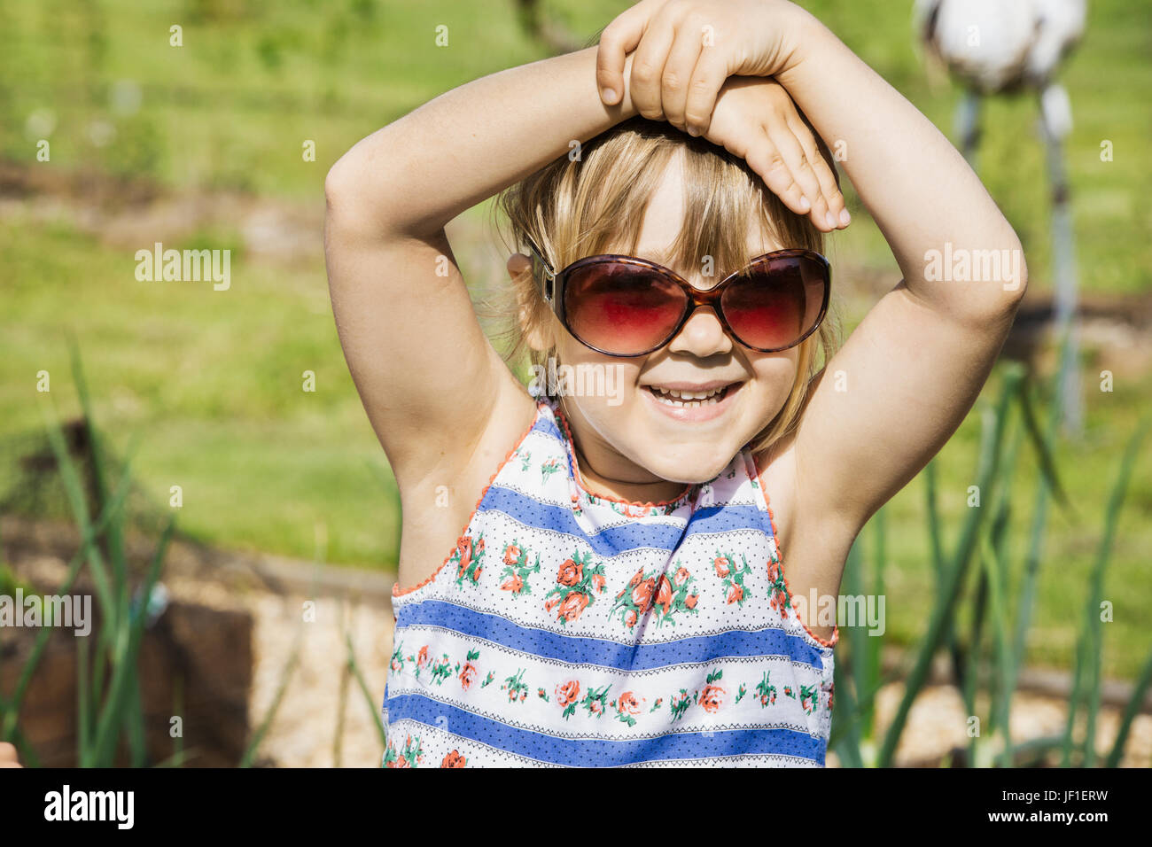 Mädchen in einem Sommerkleid tragen Sonnenbrillen, Hände am Kopf, lächelt in die Kamera. Stockfoto