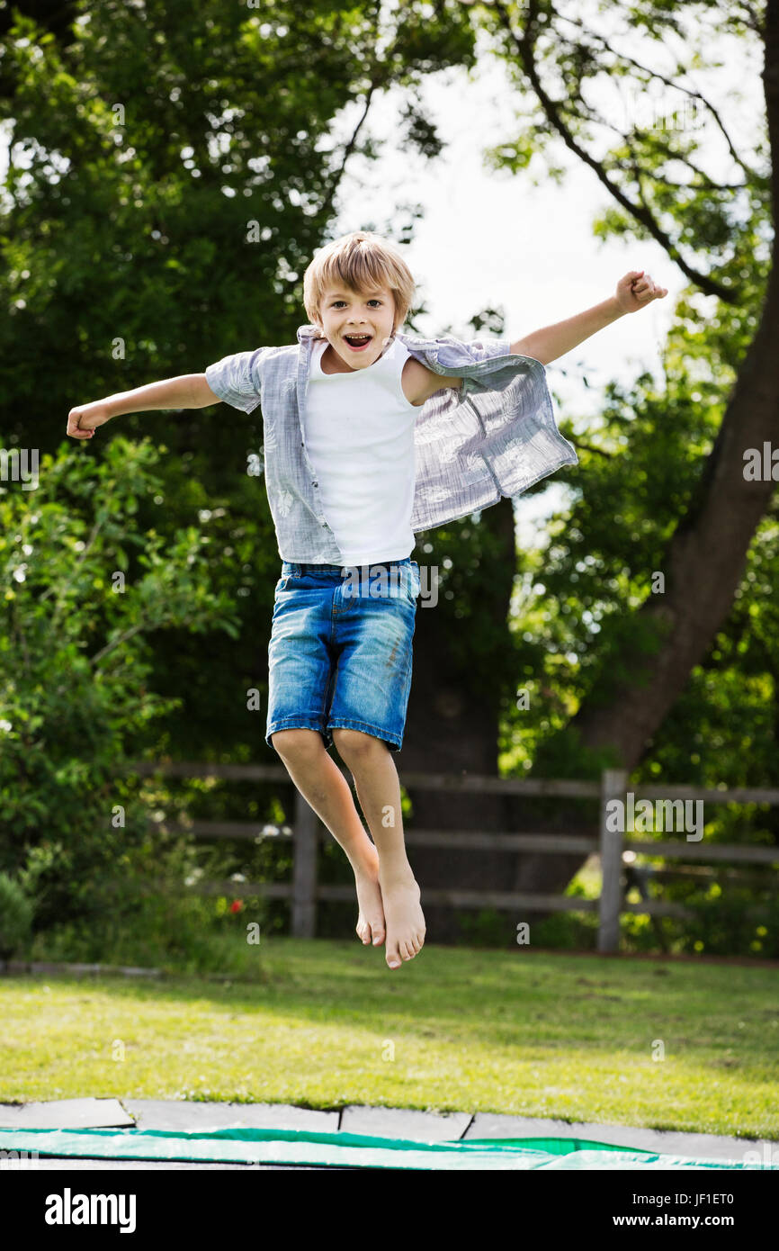 Jungen tragen Hemd und Jeans-Shorts, springen auf einem Trampolin im Garten. Stockfoto