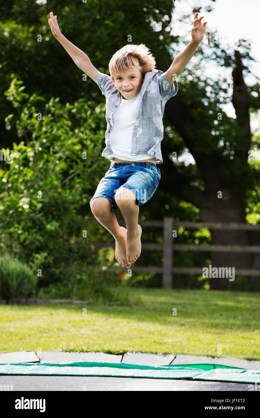 Jungen tragen Hemd und Jeans-Shorts, springen auf einem Trampolin im Garten. Stockfoto