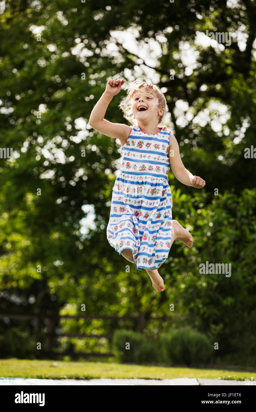 Mädchen in einem Sommerkleid, springen auf einem Trampolin im Garten. Stockfoto