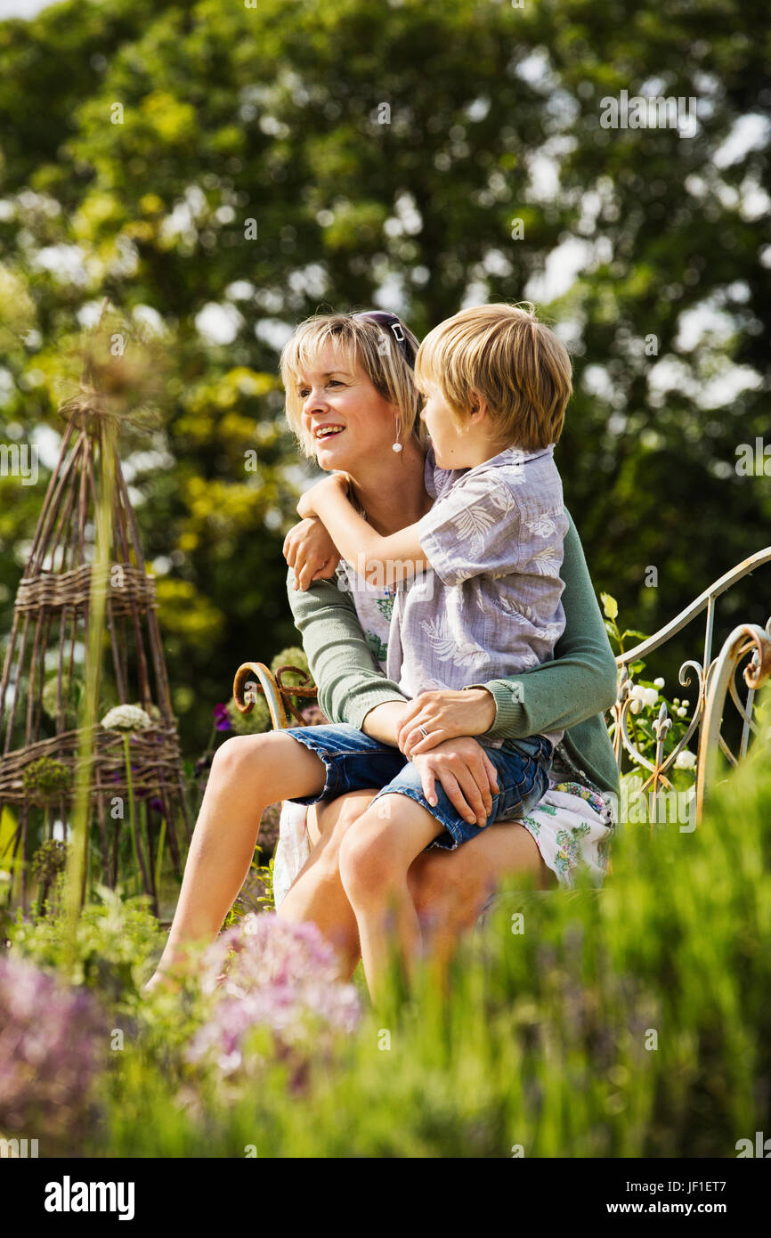 Frau sitzt in einem Garten mit einem jungen auf dem Schoß umarmt. Stockfoto