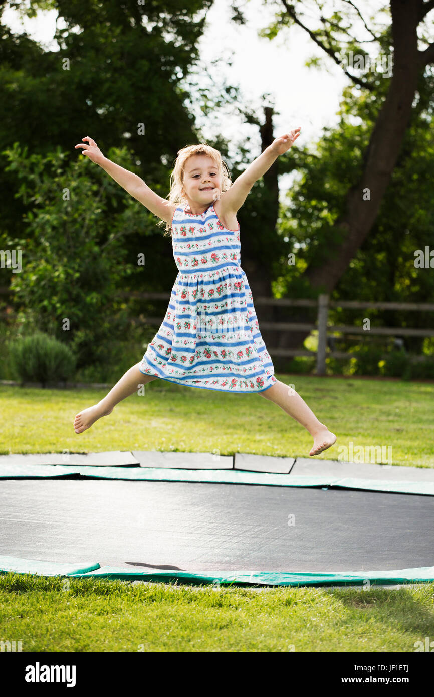 Mädchen in einem Sommerkleid, springen auf einem Trampolin im Boden, in einem Garten gesetzt. Stockfoto