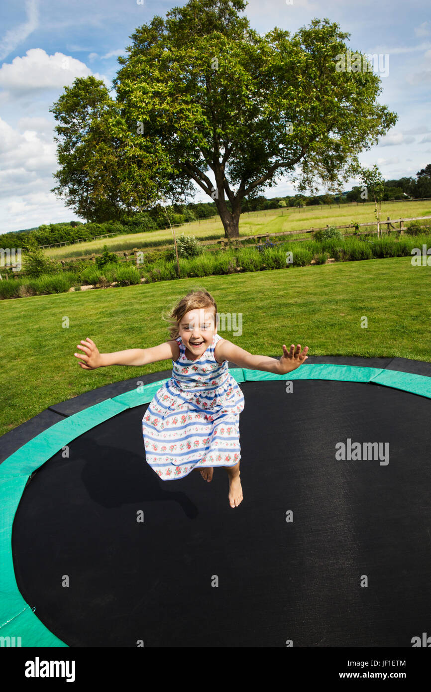 Mädchen in einem Sommerkleid, springen auf einem Trampolin im Garten. Stockfoto