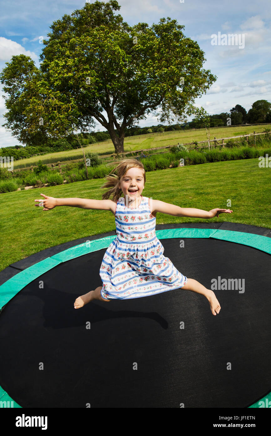 Mädchen in einem Sommerkleid, springen auf einem Trampolin im Garten. Stockfoto