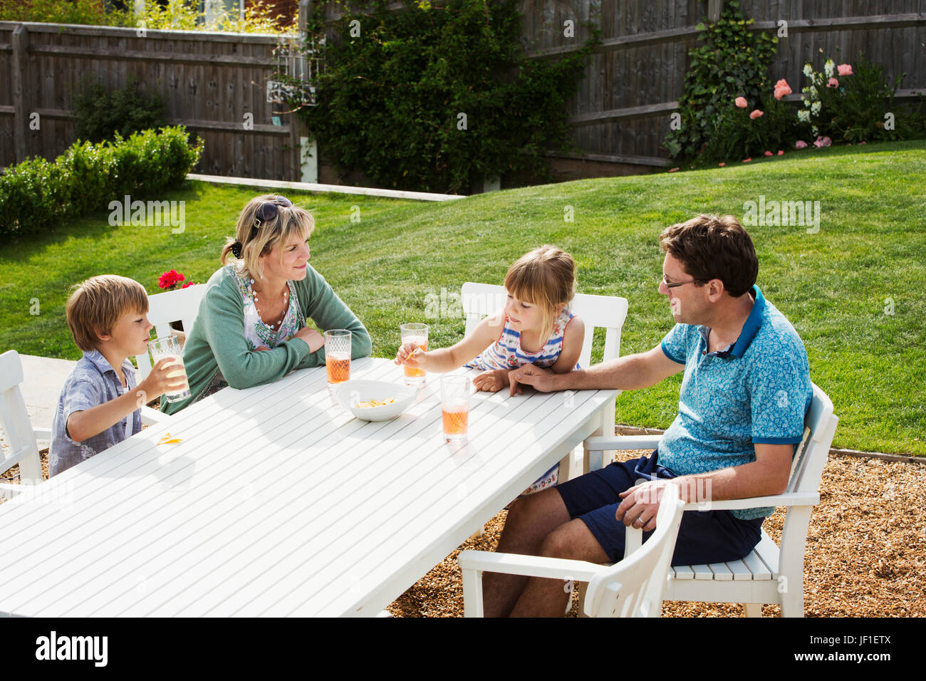 Eine Familie sitzt auf einem Gartentisch, Eltern und zwei Kinder, einen jungen und ein Mädchen. Stockfoto