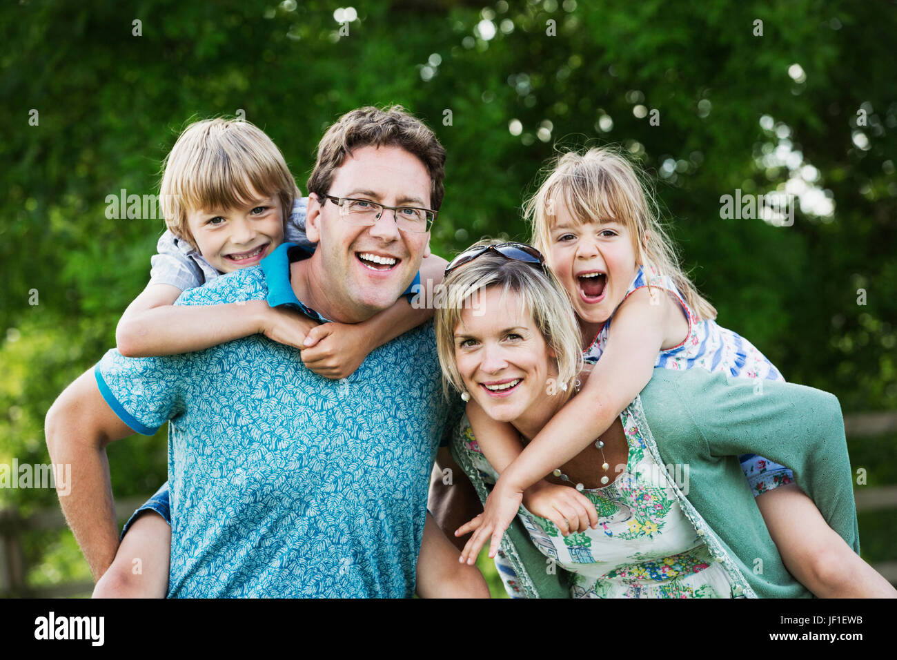 Eltern, ein Mann und eine Frau in einem Garten stehen, ihren Sohn und Tochter Huckepacks geben. Stockfoto