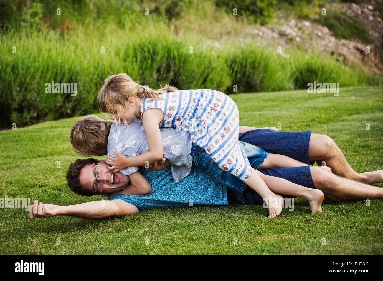 Ein Mann liegt auf dem Rasen mit seinen beiden Kindern liegen oben auf ihm spielen. Stockfoto
