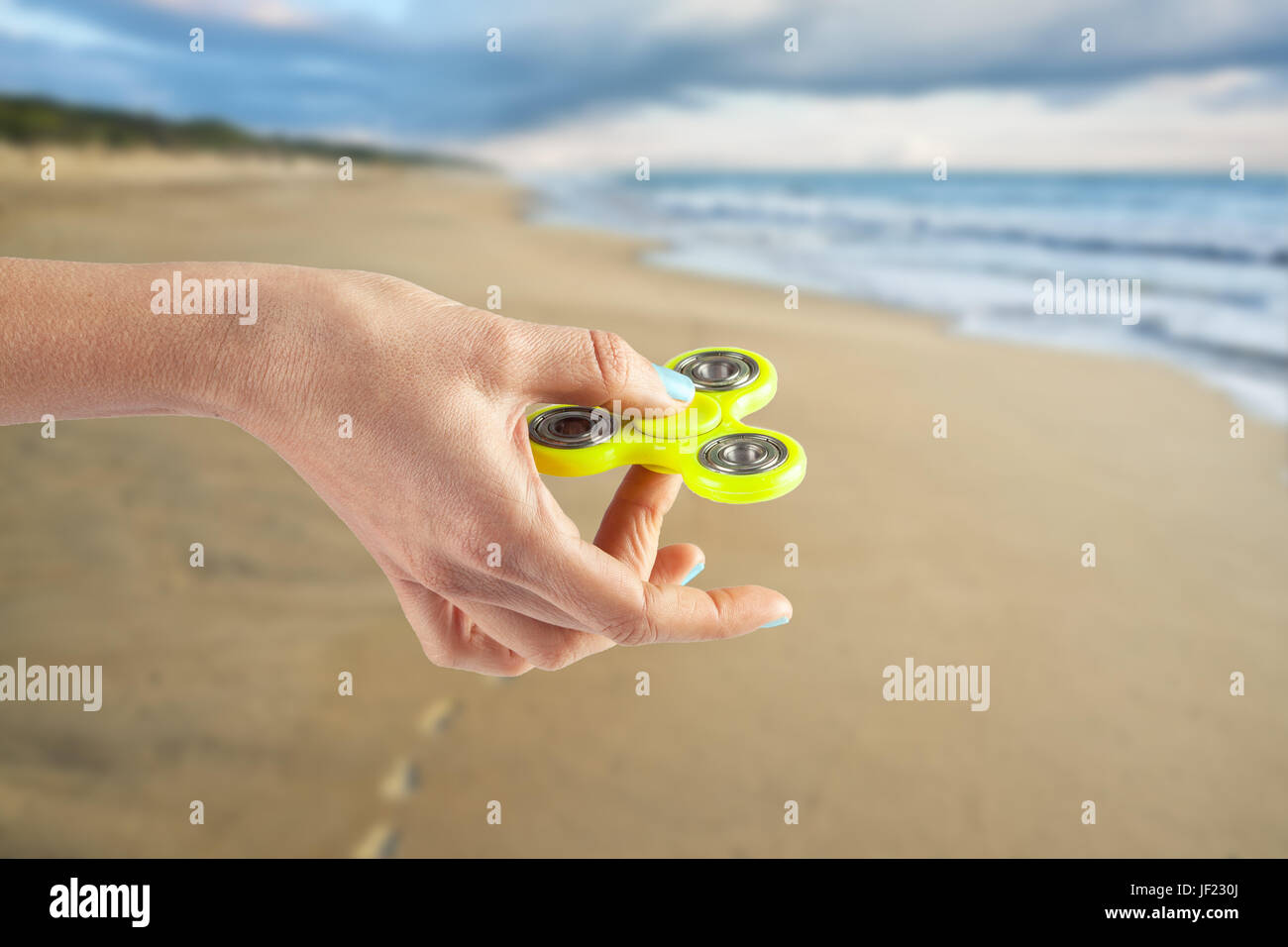 Weibliche Hand, die gelbe Fidget Spinner auf unscharf Hintergrund von Ocean beach Stockfoto