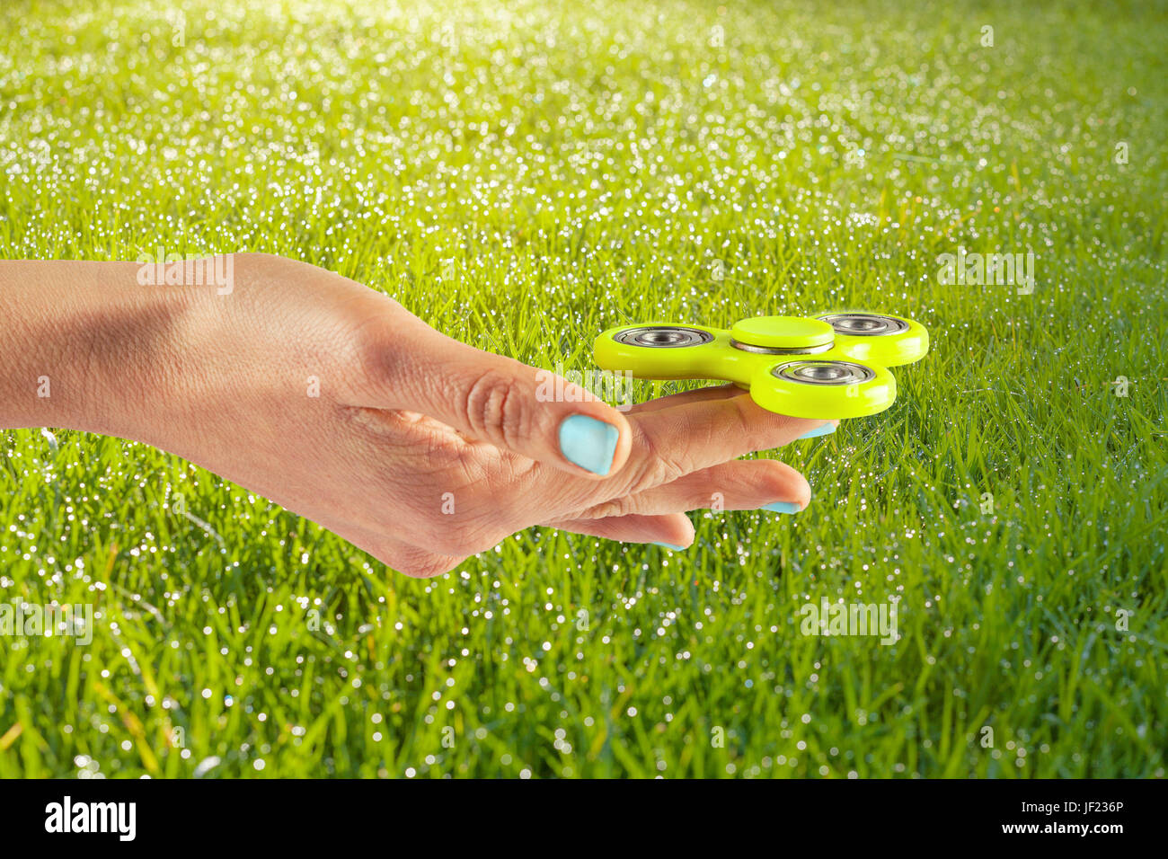 Weibliche Hand Holding gelb zappeln Spinner auf einem grasigen sonnigen Hintergrund Stockfoto