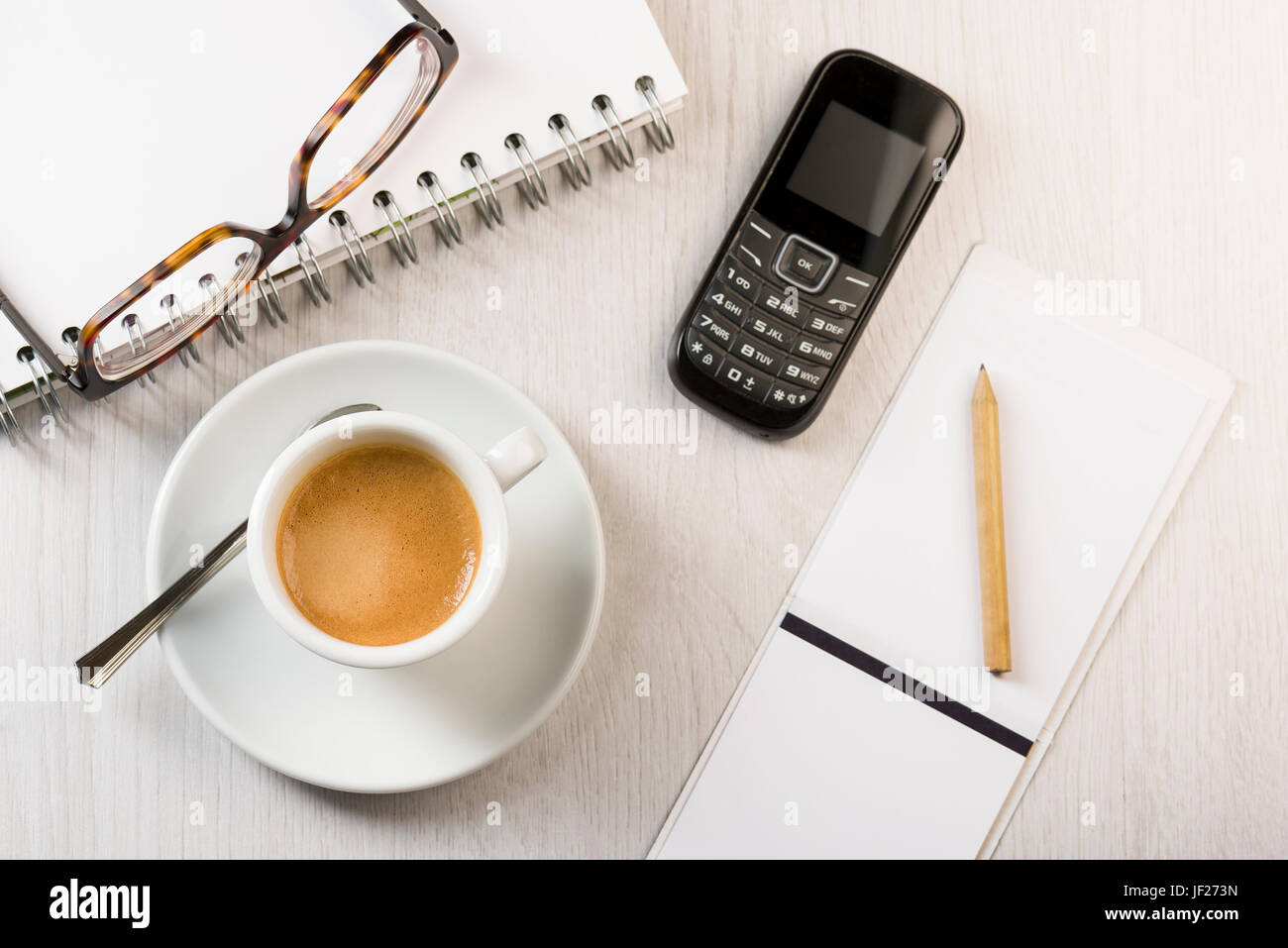 Tasse Kaffee auf weißer Bürotisch mit Noten, Bleistift, Telefon und Brillen. Stockfoto