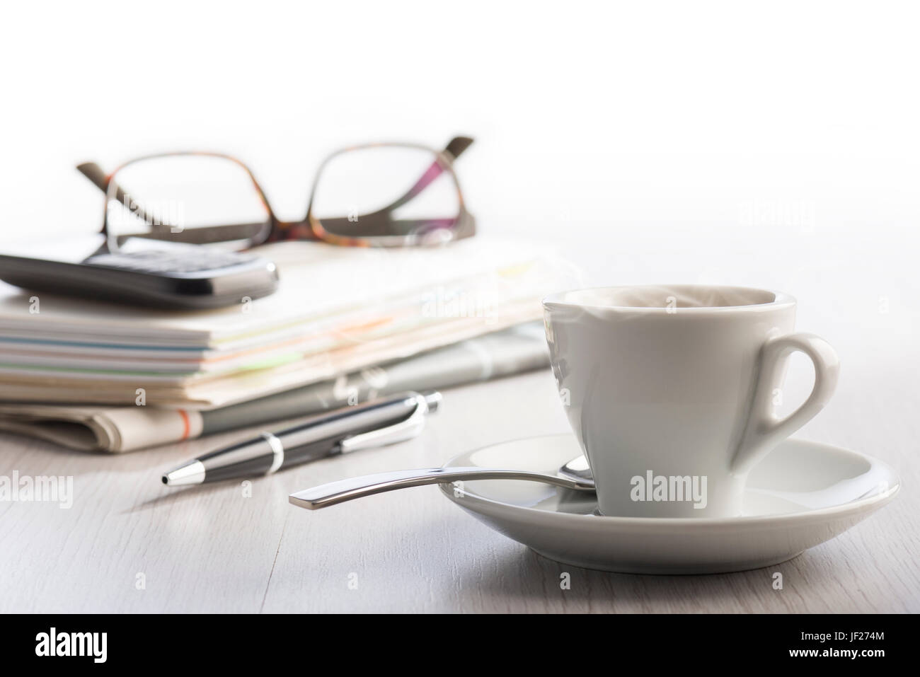 dampfende Tasse Kaffee auf weißer Bürotisch mit Noten, Handy, Brillen und Kugelschreiber auf Hintergrund. Stockfoto