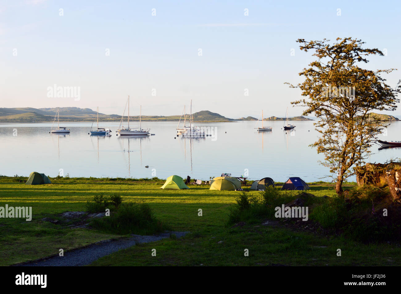 Segelboote vor Anker in der Nähe des Campingplatzes in Merchiston, Small Isles Bay in der Dämmerung auf der Isle of Jura in den schottischen Inseln, Schottland, Vereinigtes Königreich. Stockfoto
