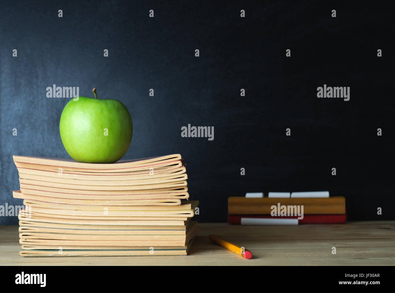 Eine Lehrerin Schreibtisch mit Stapel Hefte und Apfel im linken Frame. Eine leere Tafel im Hintergrund weichzeichnen Eingabefeld kopieren. Stockfoto