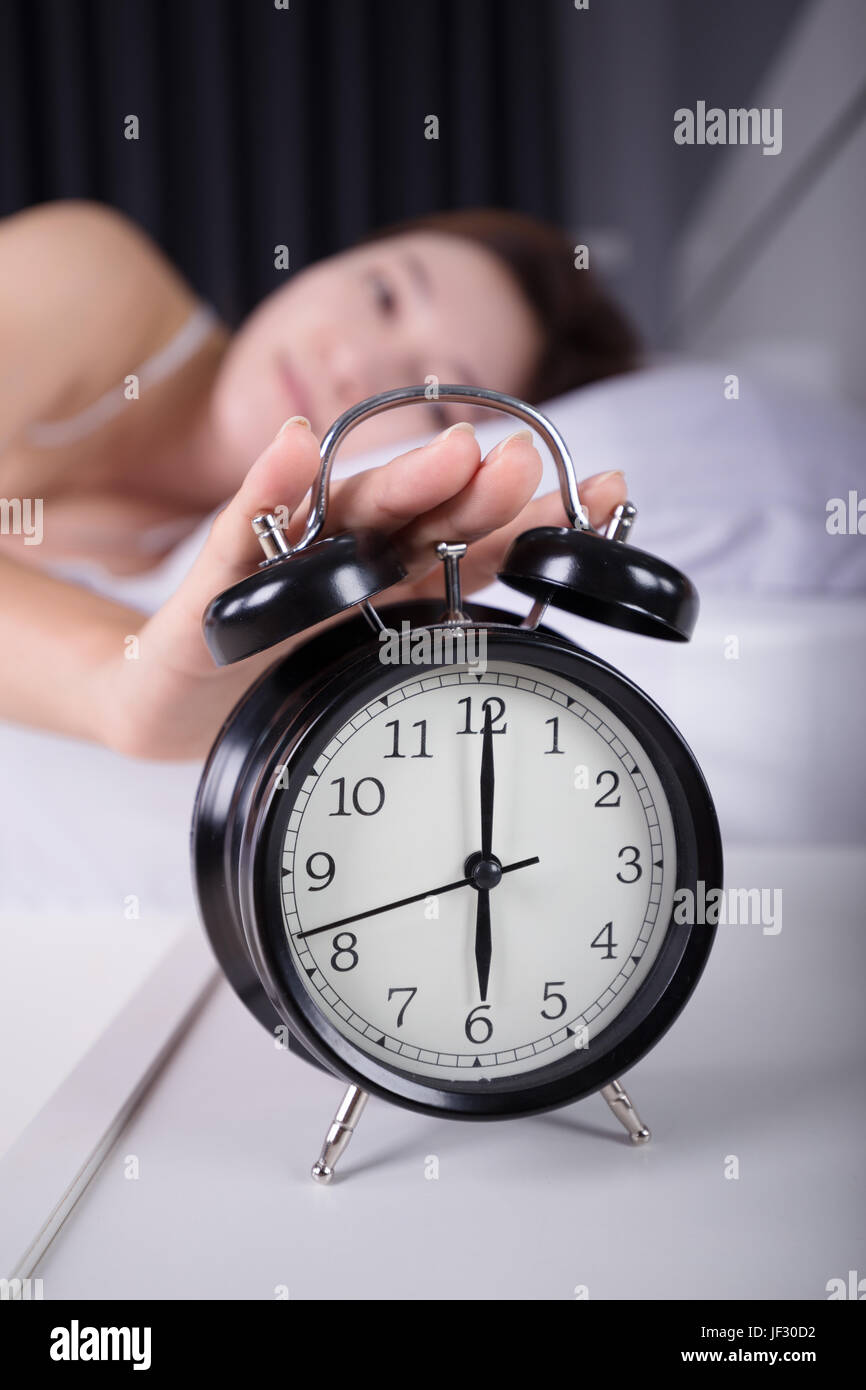 Frau schlafen und Aufwachen bis zum Ausschalten des Weckers morgens Stockfoto