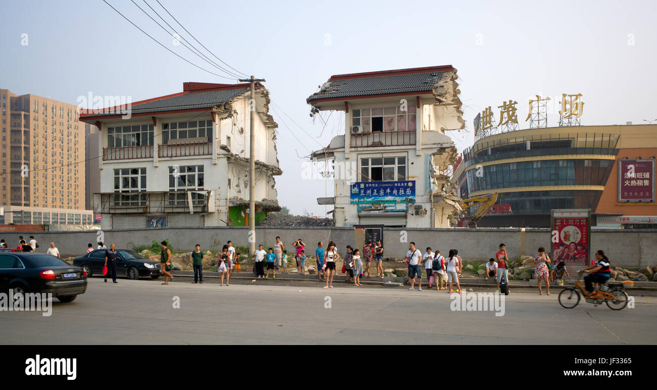 Die beabsichtigen, Fahrgäste an der Haltestelle wartet mit 'nail House' Widerstand gegen die Entwicklung und Shimao Plaza Einkaufszentrum hinter, Xuzhou, Jiangsu, China Stockfoto