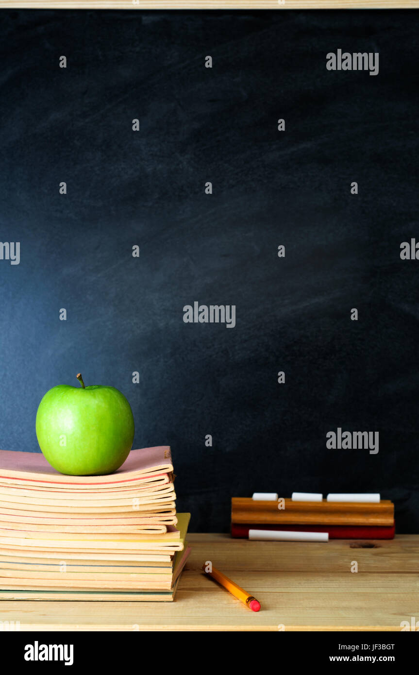 Eine Schule-Tafel und Lehrerpult mit Stapel Hefte und einen Apfel. Kopieren Sie Platz auf der Tafel.  Im Hochformat (vertikal). Stockfoto
