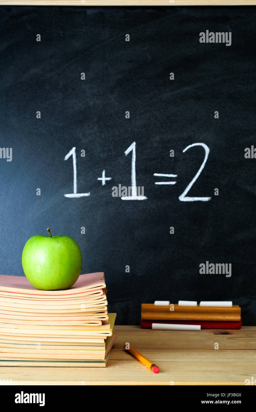 Eine Schule-Tafel und Lehrerpult mit Stapel Hefte und einen Apfel.  Die Summe "1 + 1 = 2' wird an die Tafel geschrieben. Stockfoto