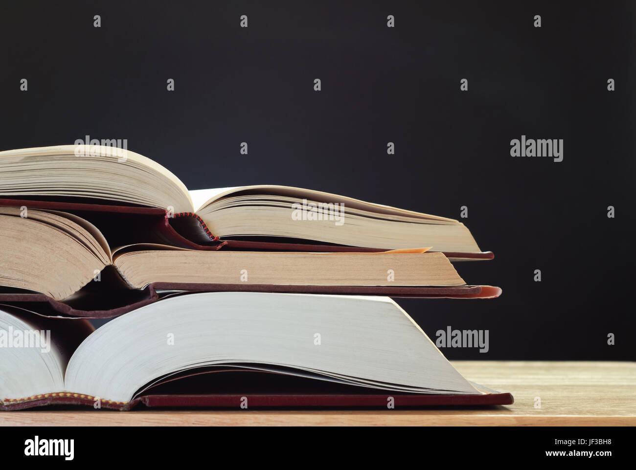 Ein Haufen von drei geöffneten Büchern auf dem hellen Holz Schreibtisch, mit einer Tafel (Tafel) im Hintergrund für Textfreiraum.  Landschaft (Horizontal) orientatio Stockfoto