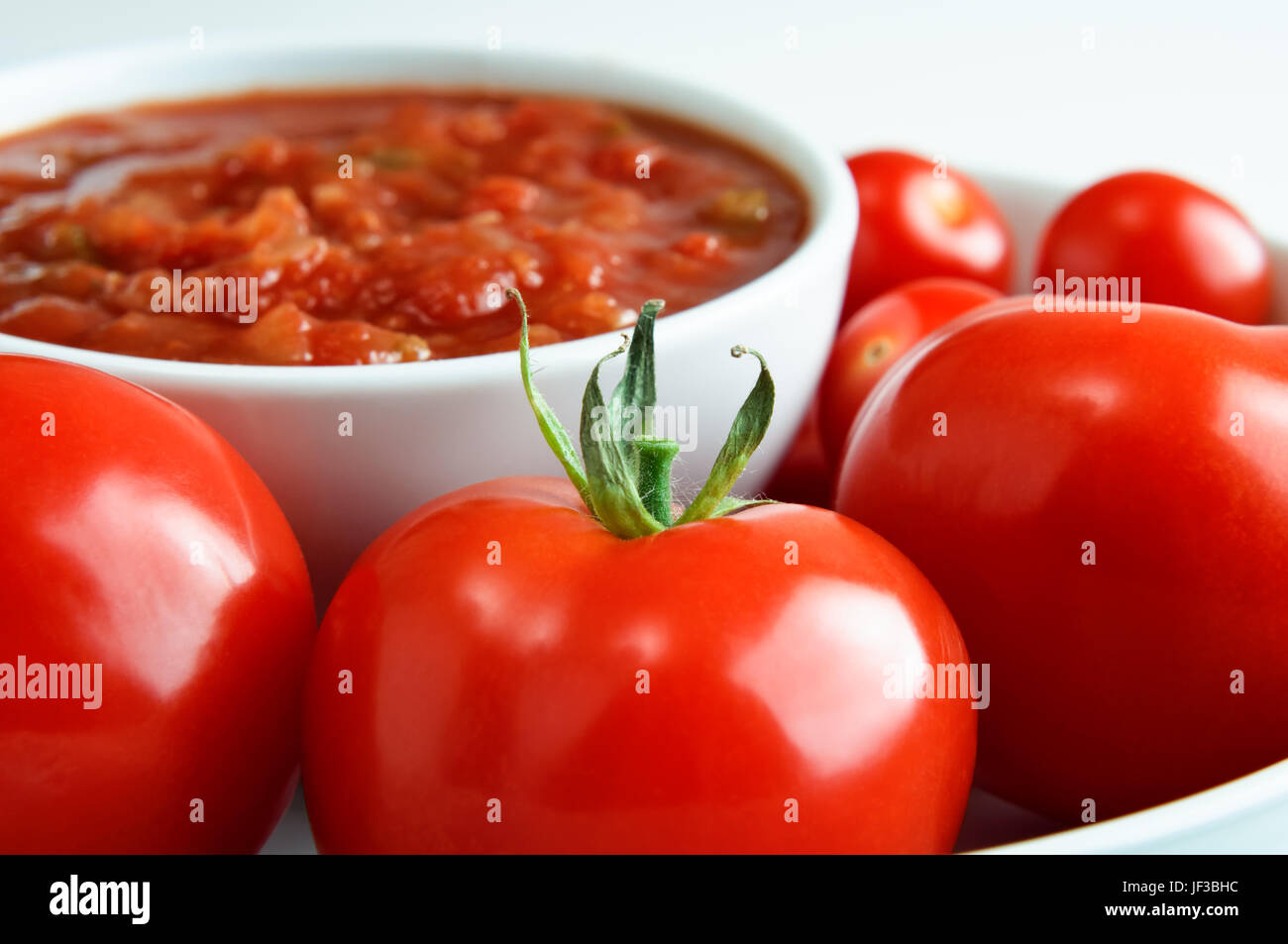 Nahaufnahme (Makro) leuchtend rote Tomaten, rund um eine Schüssel mit Salsa in soft-Fokus im Hintergrund.  Horizontal (Querformat) Orientierung. Stockfoto