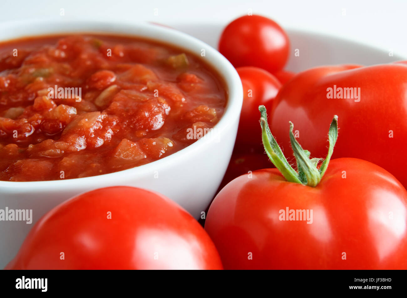 Eine weiße China Schüssel mit roter Salsa, umgeben von frischen Tomaten.  Querformat (horizontale). Stockfoto