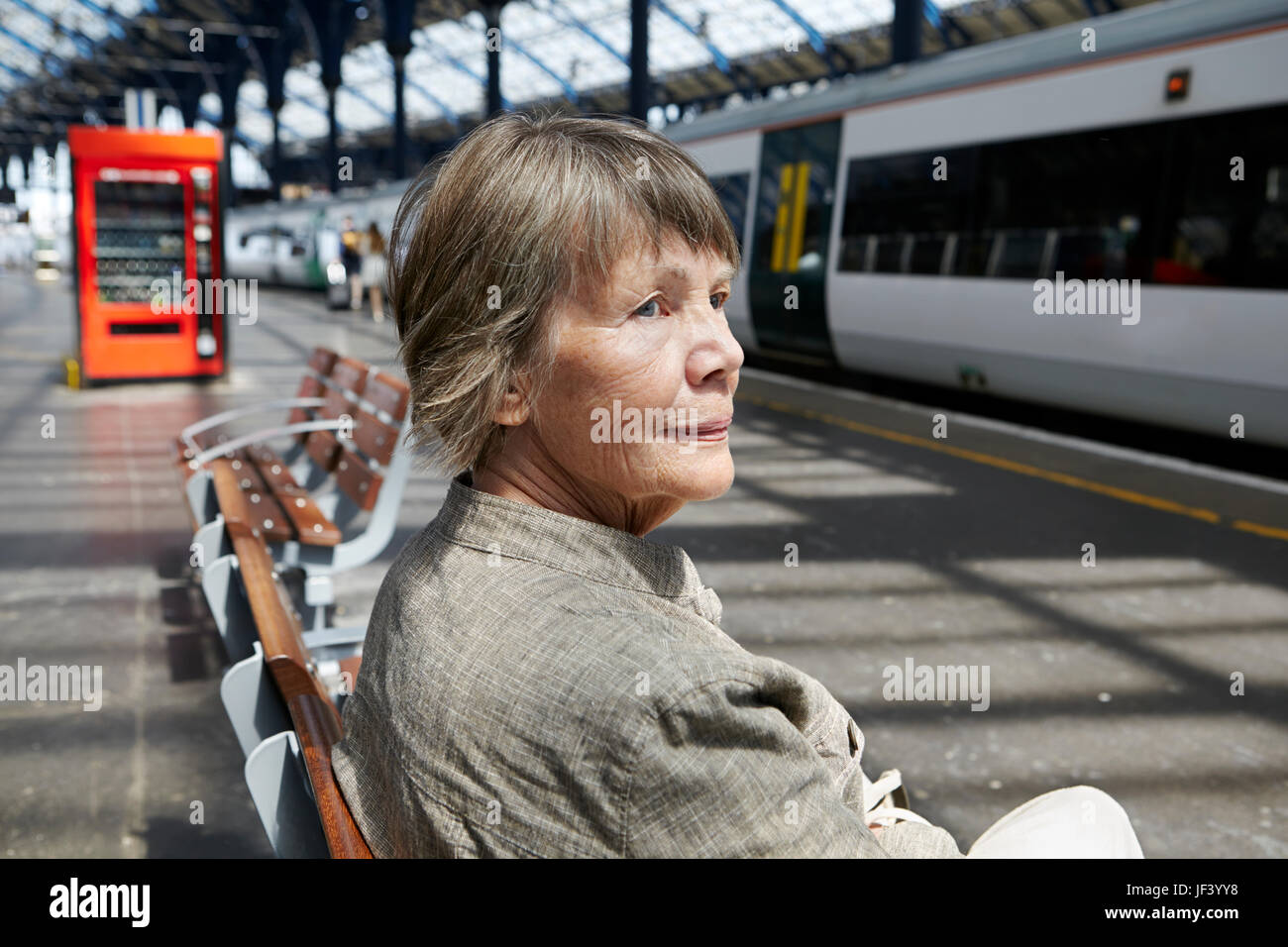 Ältere Frau sitzt am Bahnhof Stockfoto