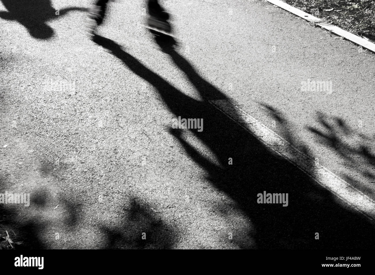 Abstrakte verschwommenen Schatten und Silhouetten von zwei Kindern, die Beschleunigung auf Rollerblades jagen einander und Spaß an der Park Lane in den Sommerferien Stockfoto
