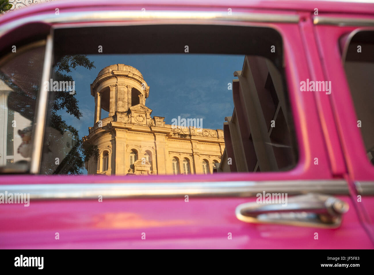 Kubanische Architektur spiegelt sich im Fenster eines bunten amerikanischen Oldtimers. Stockfoto