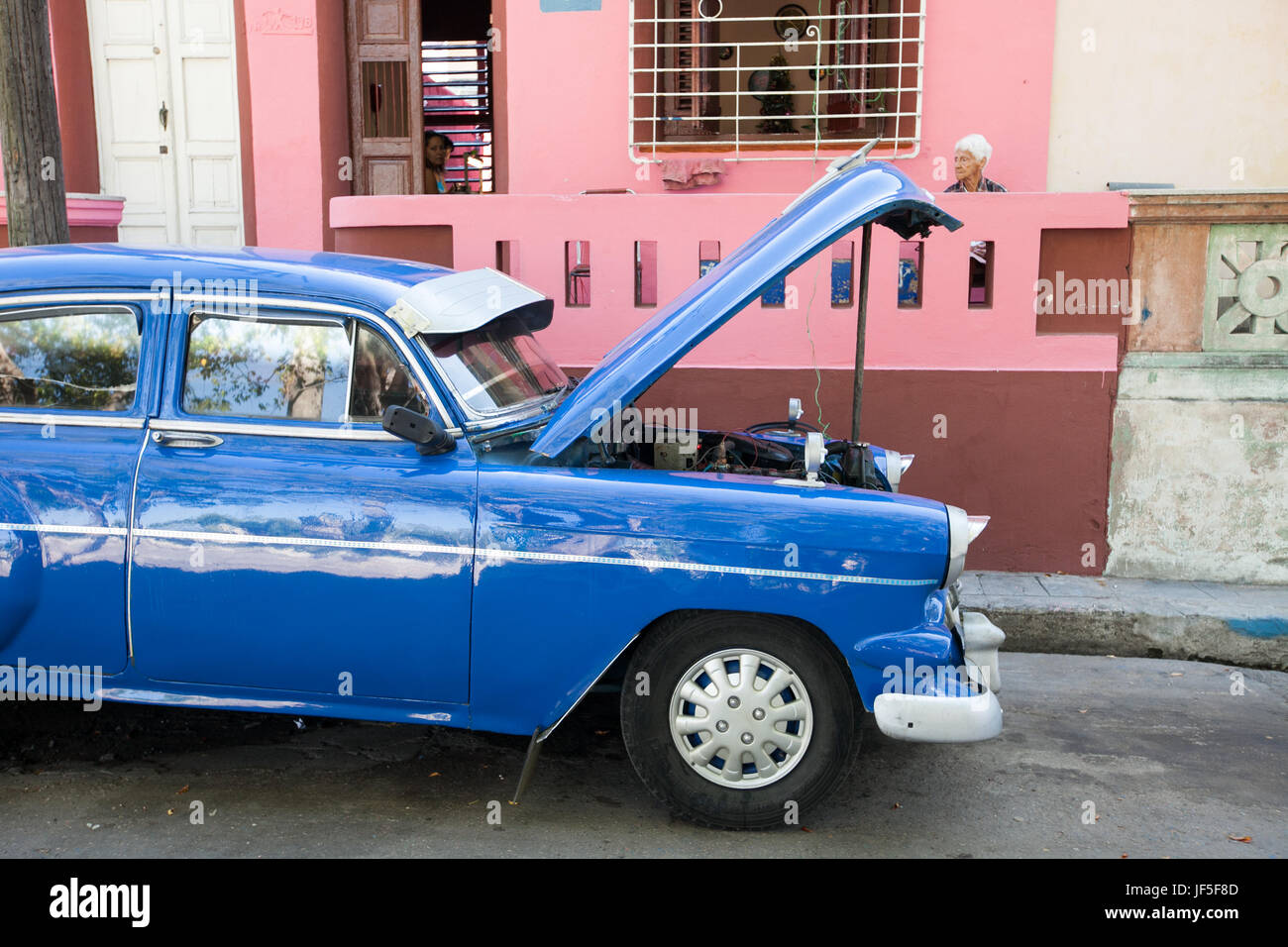 Auf den Straßen der Innenstadt von Havanna ist die Haube eines amerikanischen Oldtimers für Wartung angehoben, während Leute um das Haus herum sitzen. Stockfoto