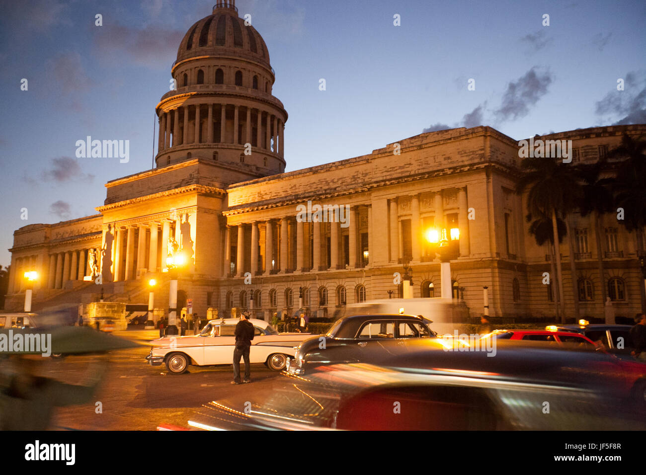 In der Abenddämmerung, außerhalb des Gebäudes El Capitolio beleuchten Lichter eine Straße, die mit klassischen amerikanischen Autos gefüllt ist. Stockfoto