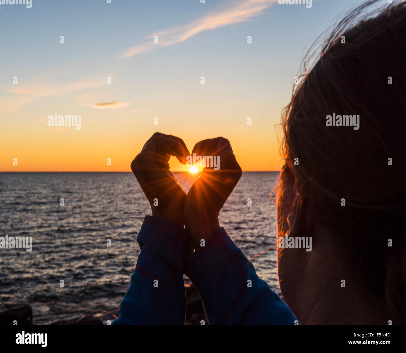 Frau macht Herzform bei Sonnenuntergang Stockfoto