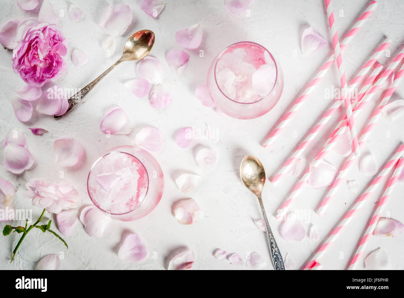 Sommer erfrischende Desserts. Vegane Ernährung essen. Eis, gefrorene rose, erstarrte und mit Rosenblättern und Roséwein. Weiße Betontisch mit Löffeln, gestreift Stockfoto