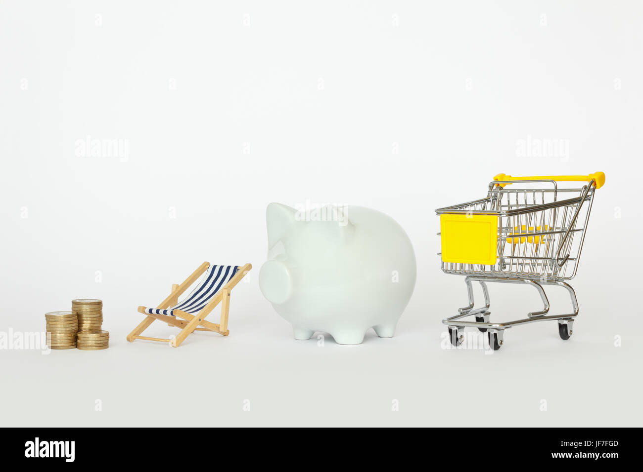 Ein Stapel von Münzen mit Liegestuhl, Sparschwein und einem Warenkorb auf weißem Hintergrund, Copyspace Stockfoto